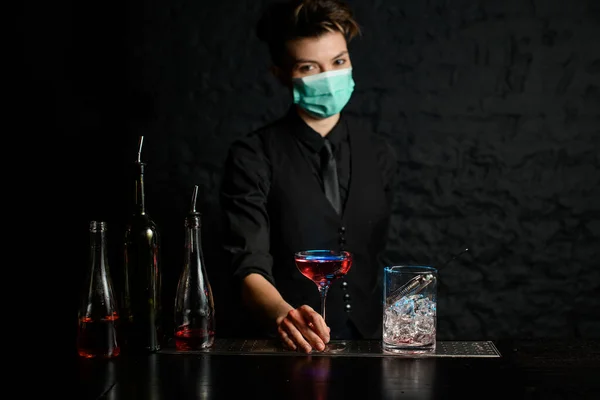 Barman en traje negro y máscara médica de pie en el bar . — Foto de Stock