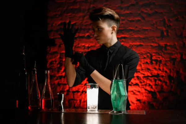 Young bartender at dark bar puts on black medical gloves — Stock Photo, Image