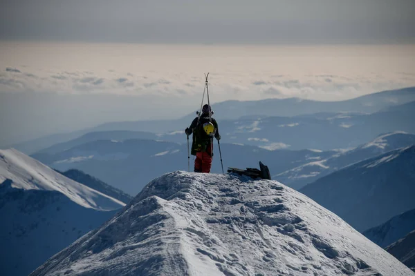 Un homme équipé de matériel de ski se tient au sommet d'une montagne enneigée . — Photo