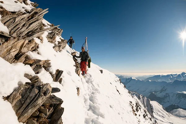 Mannen met ski-uitrusting gaan van de berg af via een sneeuwpad — Stockfoto