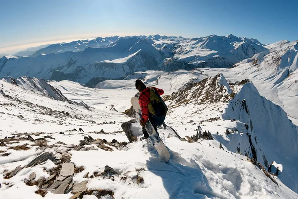 Man met snowboard in zijn handen gaat van besneeuwde berg — Stockfoto