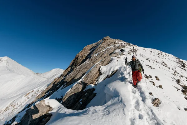 Un uomo con attrezzatura da sci sale sulla montagna innevata . — Foto Stock