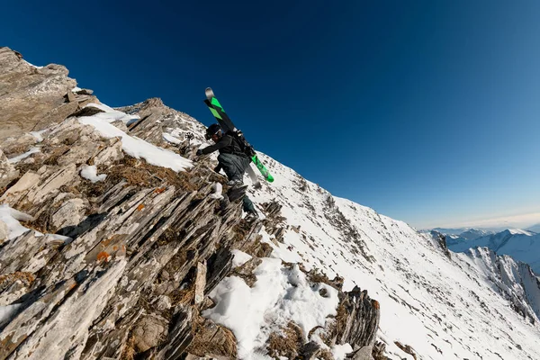 Sırtında kayak ekipmanı olan bir adam kayalık dağa tırmanıyor. — Stok fotoğraf