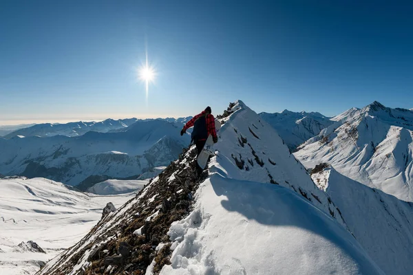 Homme avec snowboard et sac à dos monte au sommet de la montagne de pierre enneigée . — Photo