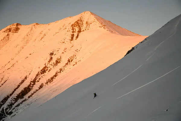 Sciatore lontano scende sul pendio della montagna al tramonto — Foto Stock