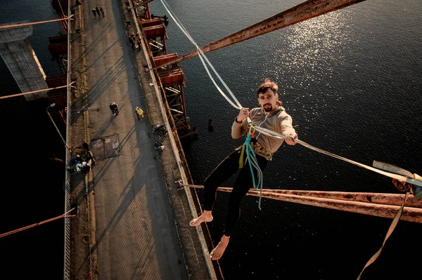 Mann mit spezieller Halterung hängt an Schlinge, die an Brücke über den Fluss gespannt ist. — Stockfoto