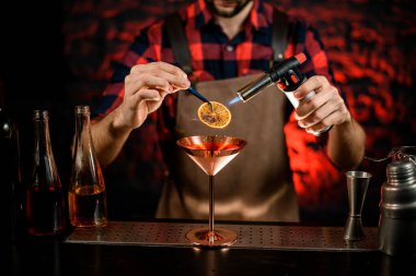 Erkek barmen, narenciye ile metal martini bardağını süslemiş ve ateşe vermiş.