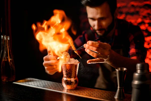 Barista tiene pinzette con spikelet sopra tazza di metallo e fa fuoco fiamma . — Foto Stock