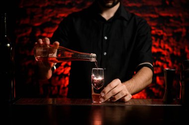 Siyah gömlekli barmen şişeden küçük bardağa kadar içiyor.