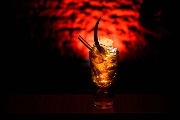Gros plan de verre avec cocktail alcoolisé lumineux décoré de tranches d'agrumes au bar sombre — Photo