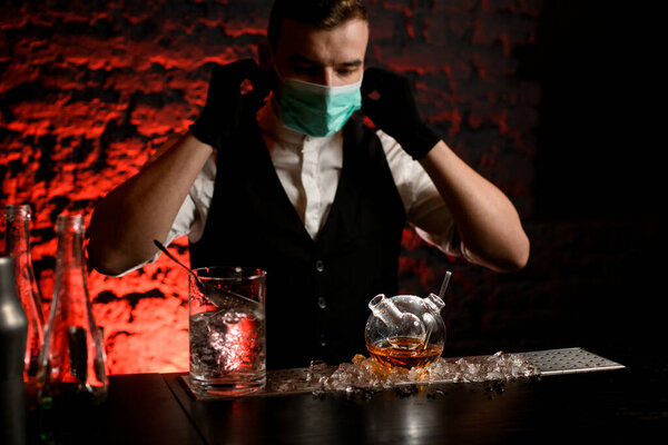 bartender in mask with black gloves drink preparing to make cocktail in special flask