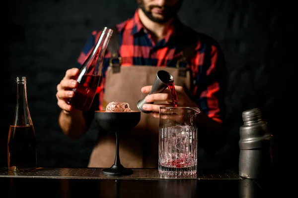 Homem barman derrama líquido vermelho de jigger em copo de mistura — Fotografia de Stock