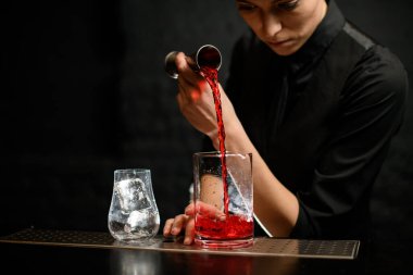 Yakın plan kadın barmen alkollü içeceği karıştırma bardağına ustalıkla dolduruyor..