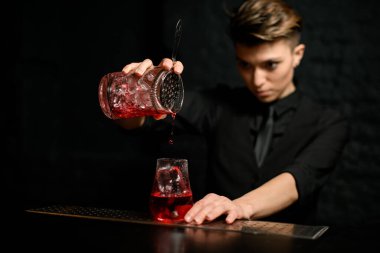 Yakın plan genç barmen kadehten süzgeci nazikçe buz bardağına koyar.