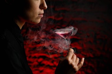 Elinde içkili dumanlı martini bardağı tutan kızın yakın profil yüzü.