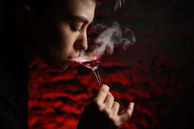 Elinde dumanlı martini bardağı tutan ve ondan içen kadının yakın plan profilli yüzü..