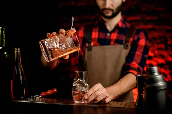 Mann Barkeeper gießt professionell Cocktail aus Mixbecher in kleines Glas. — Stockfoto