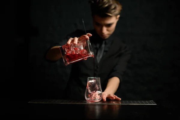 Vrouwelijke barman schenkt zachtjes cocktail uit mengbeker met zeef in glas ijs — Stockfoto