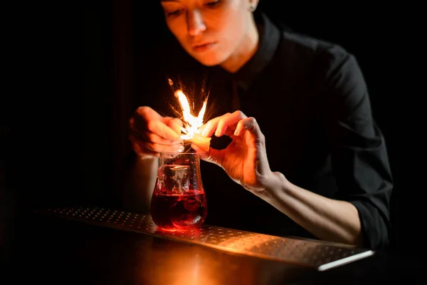 Primer plano barman espolvorea suavemente sobre vidrio con cóctel rojo y hielo y hacer fuego . — Foto de Stock