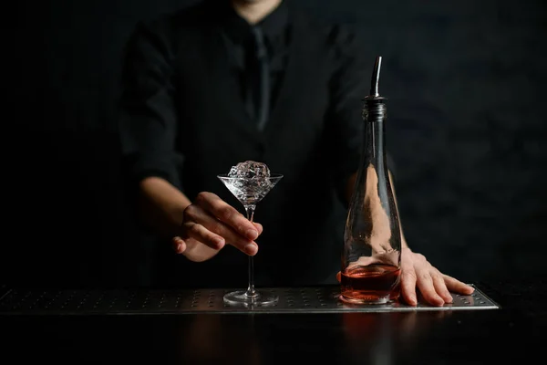 Primer plano del vaso de martini con trozo de hielo y botella en el mostrador de bar — Foto de Stock