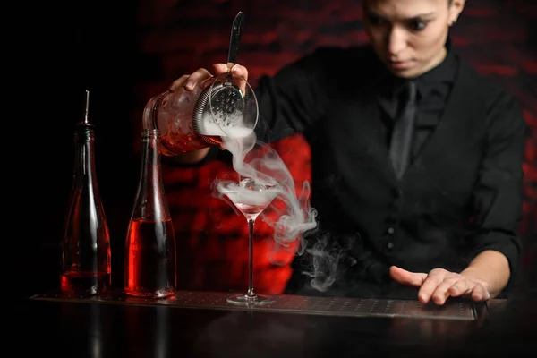 Молодая барменша нежно наливает дымящийся коктейль из смеси миски в бокал мартини . — стоковое фото