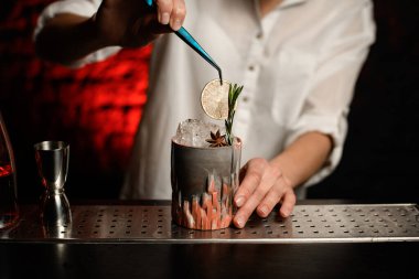 Yakın plan barmen cımbız kullanarak cam parçalarını limon dilimleriyle süslüyor.