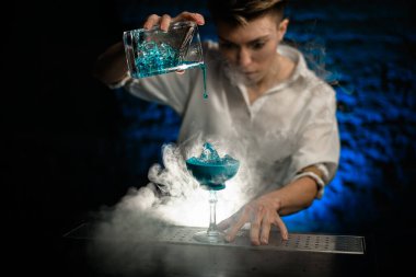 Yakın plan. Kadın barmen, Smoky Bar 'da bardağa karıştırdığı mavi kokteyli düzgünce dolduruyor ve şuna bak.