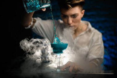 Yakın plan. Kadın barmen, Smoky Bar 'da bardakları karıştırırken dikkatli bir şekilde mavi kokteyl koyuyor ve şuna bak.