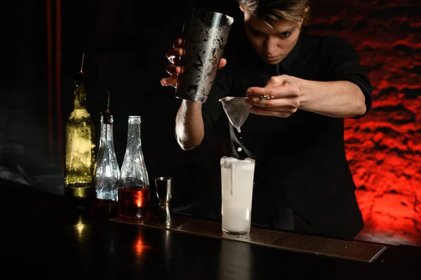 Professionele barman in donkere bar schenkt zachtjes cocktail van stalen shaker in glas — Stockfoto