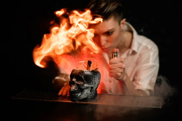 Bartender professionally sprays and makes fire flame over glass in form of black skull with ice — Stock Photo, Image