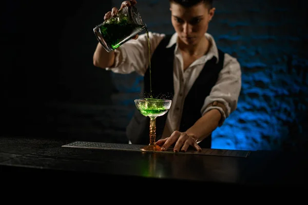 Woman bartender pours green cocktail from mixing cup into glass — Stock Photo, Image