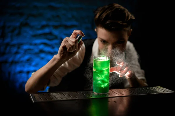 Female bartender sprinkles on glass with bright green cocktail and look at it. — Stock Photo, Image