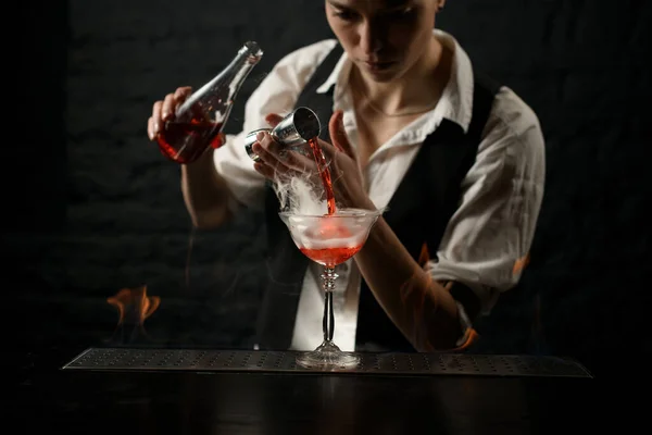 Barman profissional magistralmente derrama bebida em vidro fumado no balcão de bar . — Fotografia de Stock