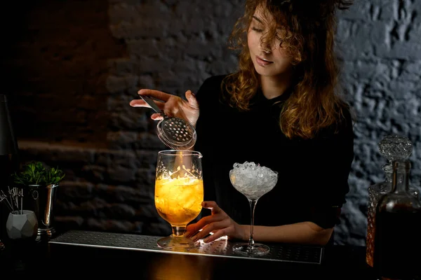 Jovem barman feminino segura filtro sobre vidro com coquetel brilhante . — Fotografia de Stock