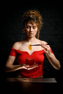 Yakın plan güzel kız elinde bardakla kokteyl ve cımbızla narenciye tutuyor..