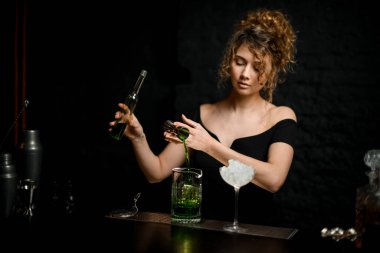 Siyah bluzlu güzel barmen kız jigger 'dan karıştırma bardağına nazikçe su dolduruyor..