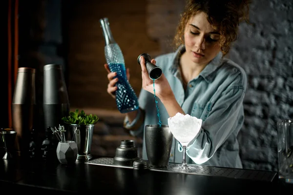 Mulher bonita bartender suavemente derrama bebida azul curaçao de jigger em shaker . — Fotografia de Stock