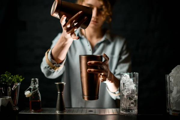 woman at bar neatly pours cocktail in steel cups