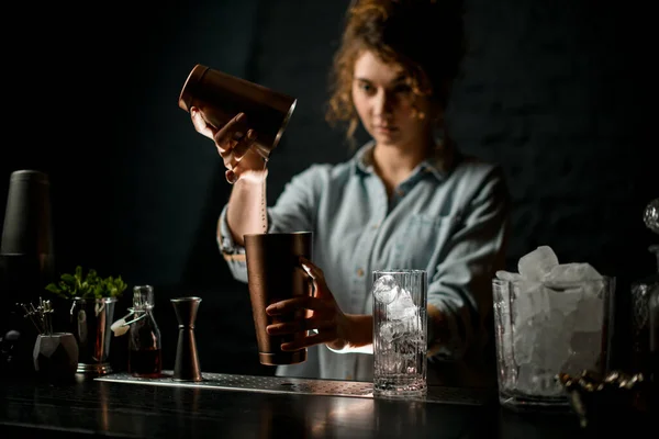 woman at bar neatly pours cocktail in steel cups and look at it.