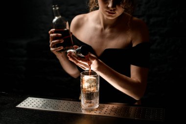 Siyah bluzlu seksi kız barmen jiggerdan bardağa nazikçe su dolduruyor..
