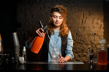 Genç barmen kız sifonla bardağa karbonatlı içecek dolduruyor..
