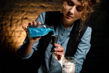 Yakın plan genç bayan barmen şişeden jigger 'a kadar içiyor.