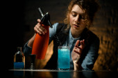 Mladý barman dívka nalévá uhličité kapaliny na sklo s modrým koktejlem.