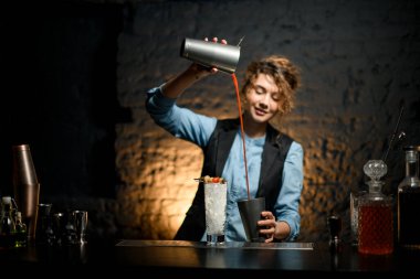 Bardaki gülümseyen kız enerjik bir şekilde turuncu kokteyl dolduruyor.