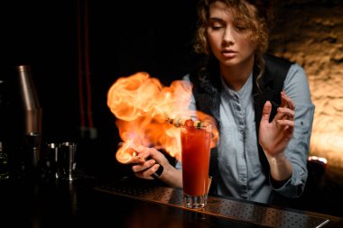 Genç barmen kız bardağa kokteyl serper ve ateşe verir..