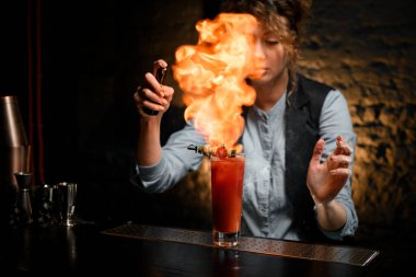 Barmen kız bardağa kokteyl serper ve ateş yakar..