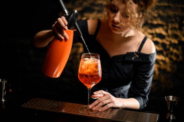 Yakın plan kadın barmen karbonatlı içeceği negroni kokteyli ile bardağa dolduruyor..