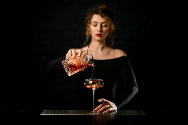Koyu bardaki kadın barmen dikkatle şarap bardağına kokteyl dolduruyor..
