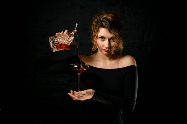 Kadın barmen elinde bardakla bardağa kokteyl dolduruyor.