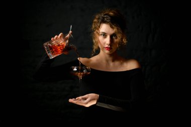 Profesyonel kadın barmen elinde bardakla bardağa kokteyl doldurur.